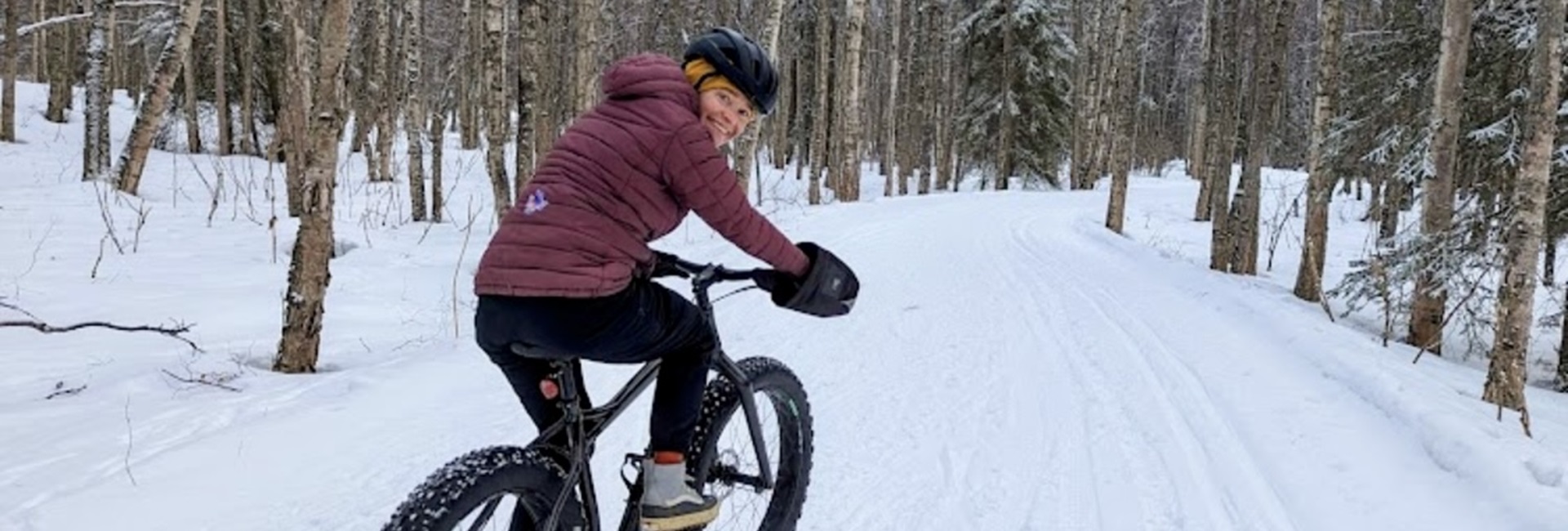 Woman biking on Anchorage Coastal Trail in winter with snow on the ground.